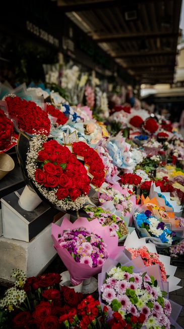 A vibrant display of floral arrangements at Romford Market showcasing an array of freshly cut flowers, including red roses, pink roses, white lilies, and colorful chrysanthemums, meticulously arranged